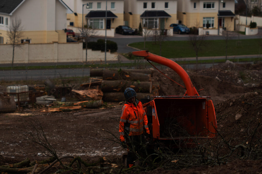 A tree surgeon standing in front of a wood chipper.